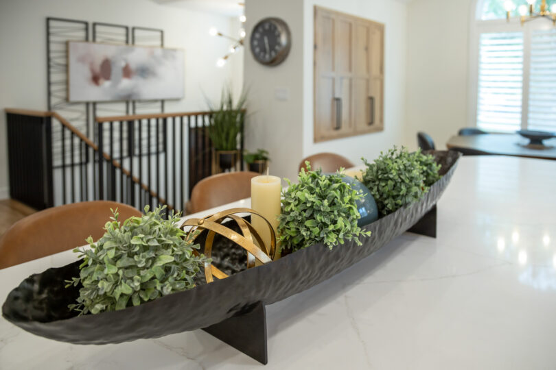 A beautifully styled kitchen island in a Fargo/Moorhead home, featuring a mix of modern and rustic elements. The island is adorned with candles and a unique centerpiece. The space is well-lit, with natural light coming from large windows, highlighting the clean countertops and minimalistic decor